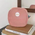 Detail view of a pink mesh square makeup bag with a BEAR logo patch sitting on books. - Yellow Orange