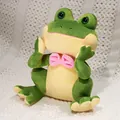 Cute green prince frog plush toy with a pink bow tie in a sitting pose. - Face-Holding Frog / 27cm