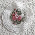 Detailed macro view of pink floral embroidery on a white European lace round coaster - Diameter 11.5cm / White
