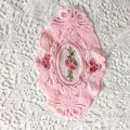 Detailansicht eines rosa ovalen Spitzenuntersetzers mit zarter Rosenstickerei auf Netz - 21*14,5 cm / Rosa