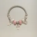 Gros plan d'un bracelet à breloques DIY avec perles roses, pendentifs cœur et nœud - Style de bracelet / Rose