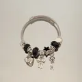 Gros plan d'un bracelet jonc en acier inoxydable avec breloques cœur, nœud et clé - Style Bracelet Jonc / Noir