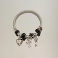 Vue détaillée d'un bracelet ouvert en acier argenté avec breloques cœur, nœud et étoile - Style de bracelet / Noir