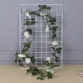 Detail view of an artificial white rose vine garland hanging on a white grid panel - White