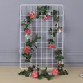 Close-up of pink artificial rose vine with green leaves on a white grid display - Orange Red