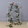Artificial pink rose garland with green leaves draped on a white metal wire grid panel - Champagne