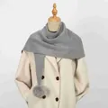 Dettaglio di sciarpa grigia a maglia con pompon decorativo su un cappotto color crema elegante - 86*36cm / Grigio