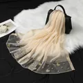 Détail d'une écharpe élégante en organza avec des broderies papillons et des perles blanches - Beige