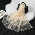 Detalle macro de un elegante pañuelo de organza con bordado de mariposas y perlas - Beige