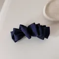 Dettaglio di un fermaglio per capelli in denim a pieghe con cuciture su sfondo neutro. - Fermaglio a banana a fiocco / Blu scuro