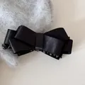 Detailansicht einer eleganten schwarzen Satin-Schleife-Bananen-Haarklammer auf Stoff - Cross Bow Banana Clip / Schwarz