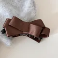 Detailansicht einer glänzenden braunen Satinschleifen-Bananenklammer auf einem Pulli. - Cross Bow Banana Clip / Braun