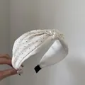 Dettaglio di un cerchietto bianco annodato con pois neri e finitura lucida satinata - Beige
