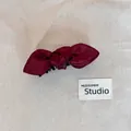 Close-up view of a deep burgundy satin bow hair clip resting on a neutral beige canvas. - Bowknot Banana Clip