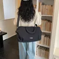 Casual black travel duffel bag with shoulder strap shown in a lifestyle library setting - Black