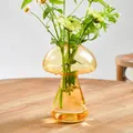 Gros plan d'un vase champignon en verre ambré avec des fleurs fraîches sur une table en bois. - Jaune