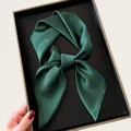 Close-up of an elegant emerald green satin square scarf tied in a bow on a black tray - 68cm / Dark Green