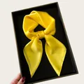 Detailed view of a vibrant yellow satin square scarf tied in a bow on a black tray - 68cm / Goose Yellow