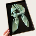 Detail shot of a soft sage green silk scarf elegantly folded in a black gift box - 68cm / Grey Green