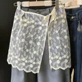 Dettaglio di un coprigonna in pizzo floreale bianco indossato su pantaloni grigi. - Taglia unica / Pantaloni e gonne / Fiori Freschi