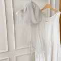 Detail of a lightweight sheer silk-like scarf with tassels hanging against a white wall - 180cm / Light Gray