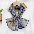 Detailed view of an ornamental paisley print thin ribbon scarf tied in a bow over white top - Blue Cashew Paisley
