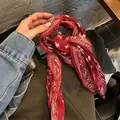 Dettaglio di un foulard vintage in seta rossa con motivo paisley usato come nastro per capelli - Borgogna