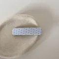 Detailopname van een blauwe stoffen haarclip met rode stippen op een beige plateau - Vierkante Snap Clip / Blauwe Stippen