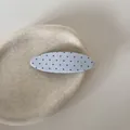 Gedetailleerd macro-aanzicht van een blauwe stoffen haarclip met rode stippen op een plateau - Ovale Snap Clip / Blauwe Stippen