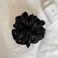 Detailopname van een zwarte satijnen oversized scrunchie met parelglans en gelaagde ruches. - Parelmoer Zwart