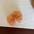 Detailed view of an orange checkered mesh bow hair clip on a clean white fabric surface - Checkered Bow Banana Clip / Orange