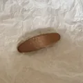 Vue macro détaillée montrant la texture d'une pince à cheveux en tissu marron - Ovale / Marron