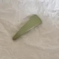 Vue détaillée d'une barrette à cheveux minimaliste en tissu vert clair sur du papier. - Triangulaire / Vert