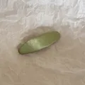 Gros plan d'une pince à cheveux BB en tissu vert sur un fond de papier beige texturé et froissé. - Ovale / Vert