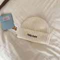 Close-up of cream knitted beanie hat with Hello Kele embroidery on soft fabric - One Size / Off White