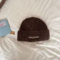 Detail view of a cozy brown knitted beanie with Hello Kele embroidery on cream fabric - One Size / Coffee