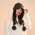 Detail view of a women's grey wool knit hat with pom-poms and earflaps in warm light - One Size / Dark Gray
