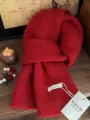 Detailansicht eines weichen roten Schals aus 100% Wolle mit feiner Strickstruktur und Tag. - Mittellanger Stil / Hellrot