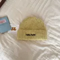 Detail shot of a yellow knitted winter beanie with black embroidery text. - One Size / Light Grass Green