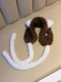 Close-up of brown and white plush cat ear earmuffs with long straps on a sofa - One Size / Brown
