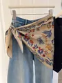Detailed shot of a vintage floral print triangle silk scarf styled as an accessory on denim jeans - Beige Flower
