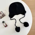 Detail view of a black wool knit beanie with pom-poms on a white lifestyle setting - M (56-58cm) / Black