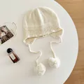 Close-up detail of a minimalist 100% wool knitted balaclava with soft white pom-poms - M (56-58cm) / White