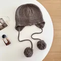 Detail view of a brown 100% wool knit balaclava hat featuring fluffy pom-poms - M (56-58cm) / Coffee