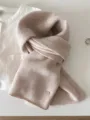 Detailed view of soft beige textured 100% wool fine knit scarf with small gold charm - 144cm / Natural Wool Color