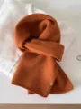 Close-up of soft burnt orange 100% wool fine knit scarf with small metal tag - 144cm / Persimmon Orange