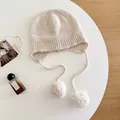 Detailed macro view of a beige wool knit beanie with soft pom-poms on a white table - M (56-58cm) / Apricot