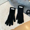Close-up macro view of black 100% wool knitted gloves showing woven material label - One Size / Black