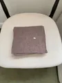 Detailed view of a brown ribbed knit scarf featuring a metal tag on a white chair - Scarf Only (Without Hat) / Coffee