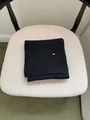 Detailed view of a black ribbed knit scarf with a small oval metal logo on a white chair. - Scarf Only (Without Hat) / Black